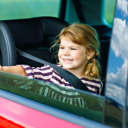 Fille adorable d’enfant en bas âge se reposant dans le siège d’auto et regardant par la fenêtre sur la nature et la circulation