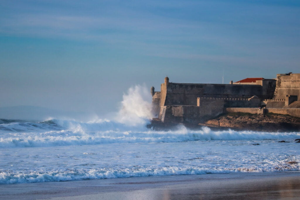 De grosses vagues s’écrasent sur une forteresse près d’une plage. Plage de Carcavelos