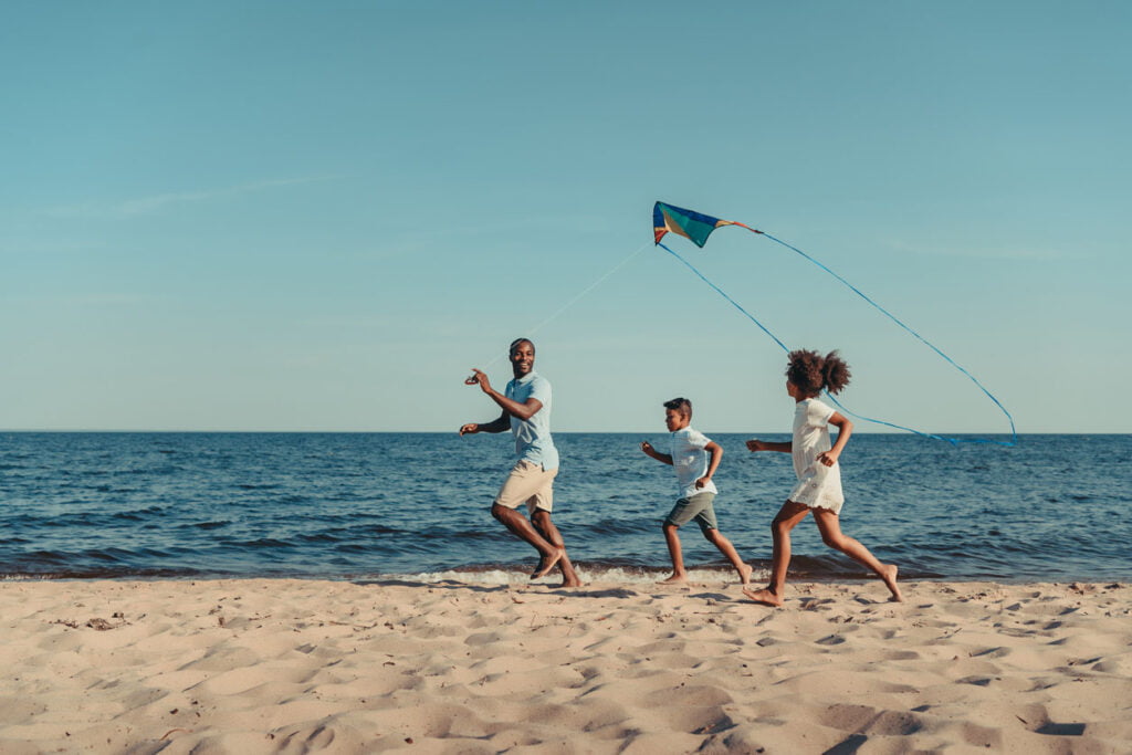 Père et enfants jouant avec cerf-volant sur la plage