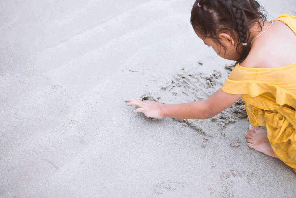 Fille enfant écrit dans le sable et joue sur la plage avec plaisir 