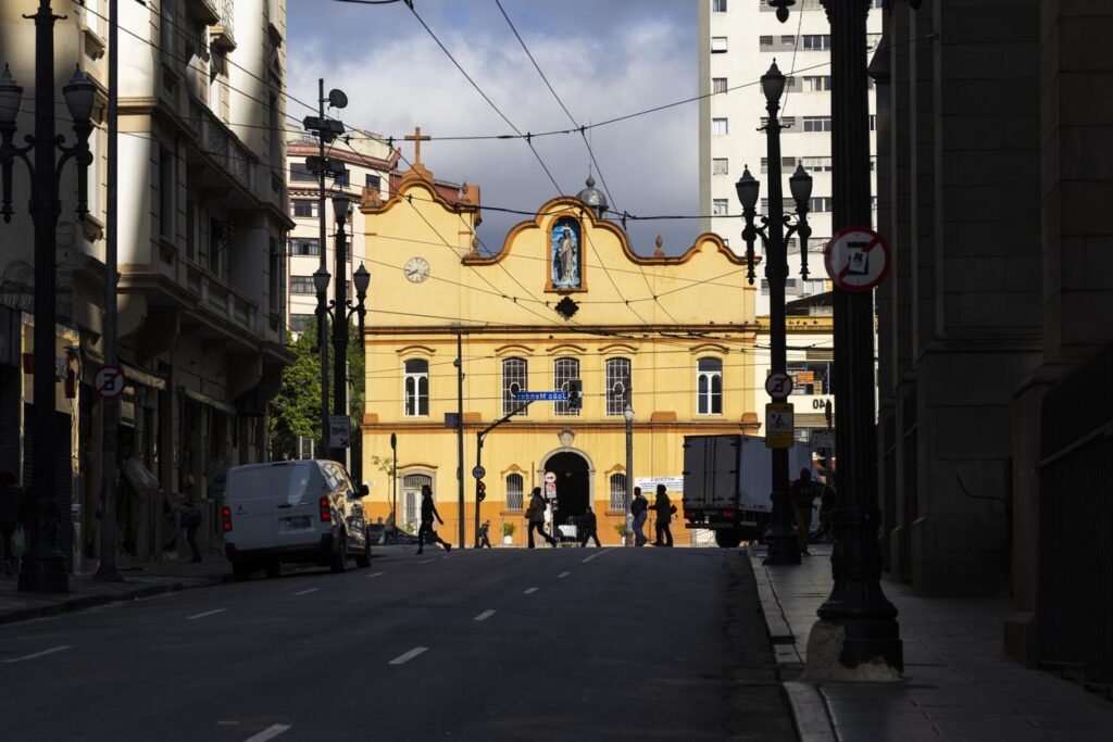 Silhouette de personnes marchant dans le centre-ville avec l’église São Miguel