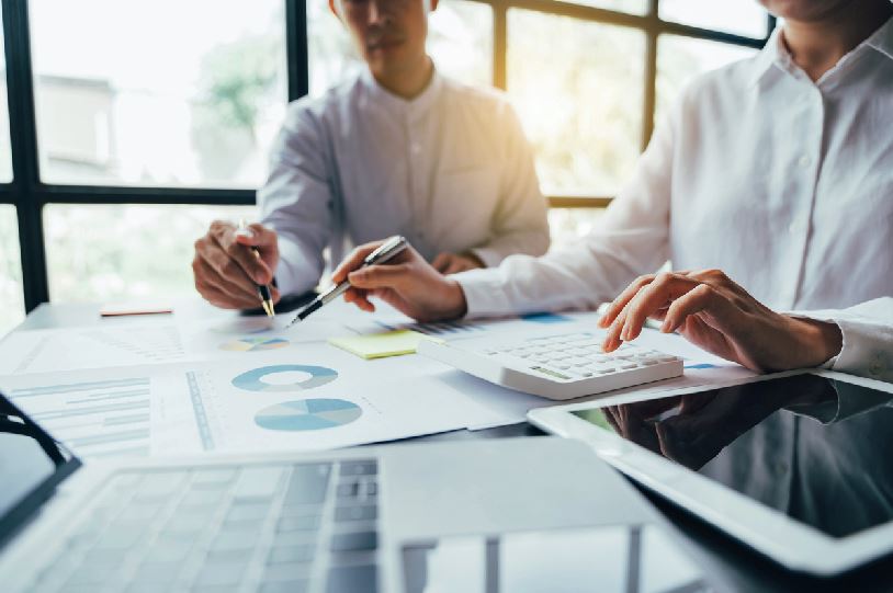 Deux Hommes Sur Un Bureau Font Des Calculs Sur Une Table, Calculatrice Et Ordinateur