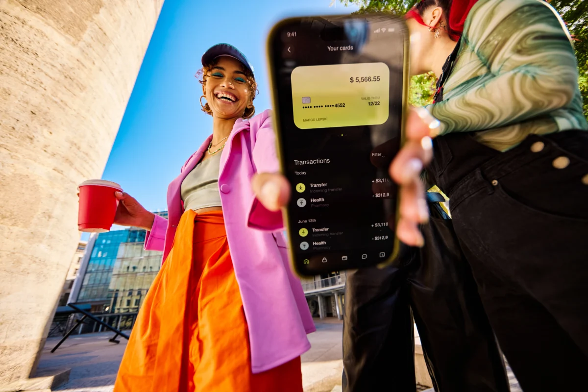 Une femme de la génération Z à l’extérieur montrant un smartphone affichant un solde bancaire et des transactions